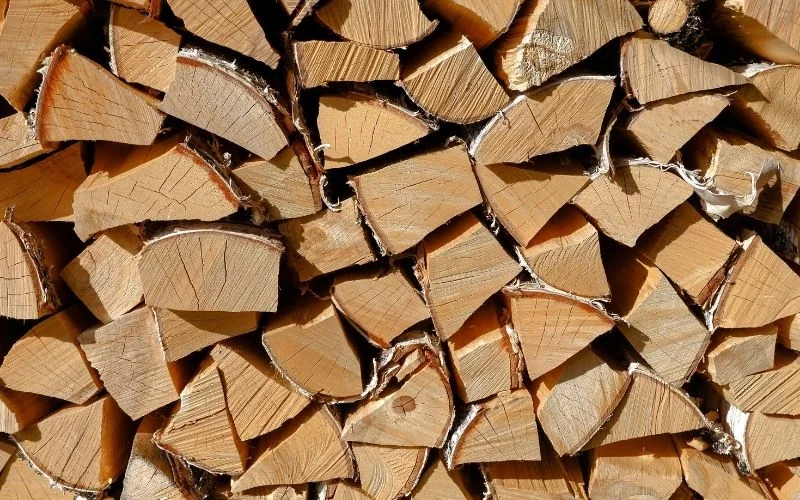 Zbliżenie na surowiec drzewny przygotowany do obróbki. Widoczne suche, porąbane polana drewna ułożone w gęsty stos, prezentujące wysoką jakość i strukturę materiału.